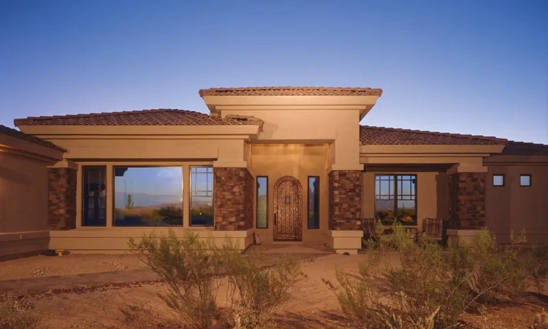A stucco home at dusk with dark fiberglass window frames